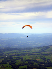 Épine mountain, France - August 5th 2008 : Focus on a purple and orange paraglider in mid flight. We can see the green countryside of the French Alps in the background.