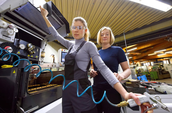 A team of two women work as computerized numerical  control engineers. They are seen together at their high  tech place of work. 