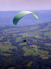 Épine mountain, France - August 5th 2008 : Focus on a green paraglider in mid flight. We can see the green countryside of the French Alps in the background.