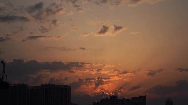 Urban silhouette with a dramatic sunset orange clouds and sun disk 