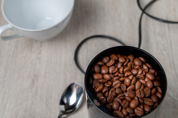 Coffee beans in a electric coffee grinder on a table with a coffee mug. Flat lay