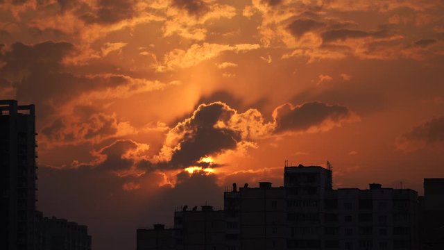Urban silhouette with a dramatic sunset orange clouds and sun disk 