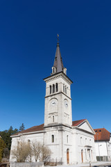 Temple de Fleurier, a beautiful white neoclassical style church with cock and bell tower against clear blue sky in the village of Val-de-Travers, Switzerland.