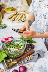 Phone picture of food. Hands make smartphone photography of summer fresh kale, cabbage salad for social media blogging. Concept for online order services. Vegan meal.