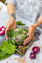 Detox vitamin green fresh salad in bowl. Mix of vegetables, sesame seeds and herbs, spinach in young woman's hands.