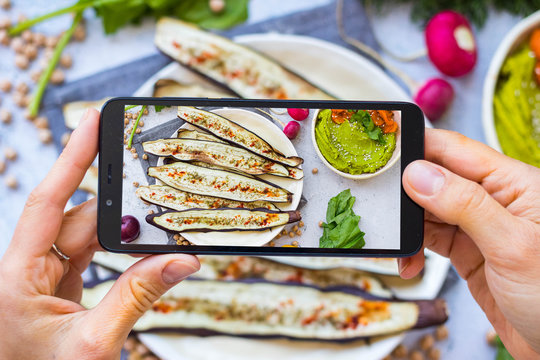 Phone picture of food. Hands make smartphone photography of grilled eggplants for social media blogging. Concept for online order services. Vegan meal.