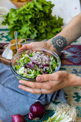 Detox vitamin green fresh salad in bowl. Mix of vegetables and herbs. Cucumbers, red onion, salad leaves salad on kitchen in woman's hands