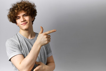 Body language. Studio shot of happy energetic young Caucasian male indicating copy space gray wall...