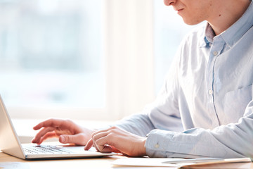 Close-up of busy man sitting at table and using laptop while analyzing internet resources