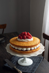 Victoria Sponge Sandwich Cake with Layers of Whipped Cream, Raspberry Jam, and Fresh Raspberries on Cake Stand in Dining Room