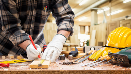 Close-up. Carpenter with his hands protected by gloves with a pencil and the meter marks the...
