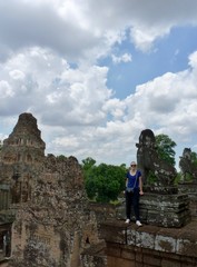 Ruins of Angkor with backpacker girl with sunglasses standing before statue, Angkor Wat, Cambodia