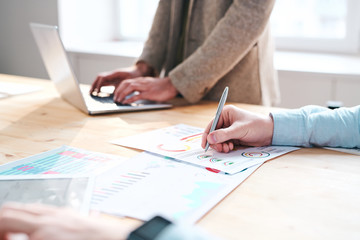 Close-up of unrecognizable financial expert making notes in chart while analyzing month report in office