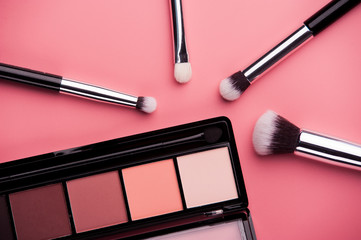 Cosmetic palette with brushes lies on a pink background