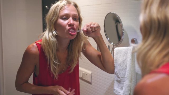 Young Blonde Woman Is Brushing Her Teeth In The Bathroom