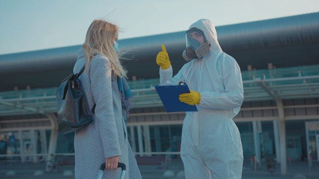 Near airport medical worker in protective suit screening passenger to check woman have temperature Covid-19 symptoms coronavirus checkpoints mask infection epidemic corona passengers slow motion