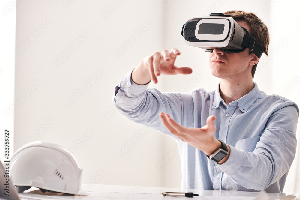 Poster Busy young architect sitting at desk and gesturing hands while creating floor plan using virtual reality goggles