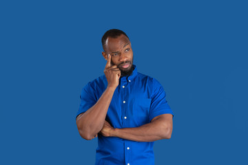 Thinking, dreaming. Monochrome portrait of young african-american man isolated on blue studio background. Beautiful male model. Human emotions, facial expression, sales, ad concept. Youth culture.