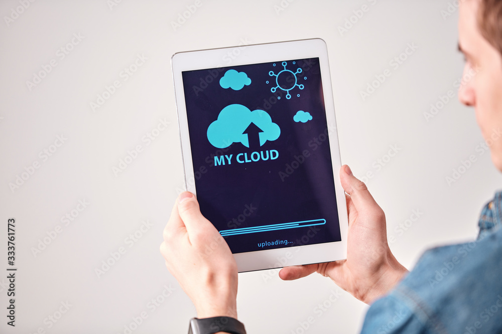 Poster Over shoulder view of young man using digital tablet while uploading files on cloud service