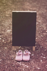 Letrero en medio de un parque con unos zapatos de bebé para anunciar próximo nacimiento: es niña