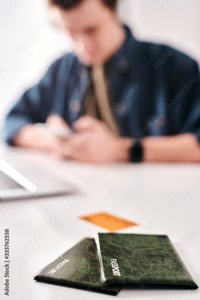 Poster Man texting message while preparing for trip in background, focus on passports in green cases on table