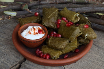 Dolma in a clay plate with pomegranate, sour cream and chacha on a wooden background