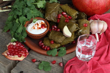 Dolma in a clay plate with pomegranate, sour cream and chacha on a wooden background