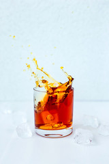 A photo of a cocktail splash, rocks glass, ice cubes around, light blue background, natural light