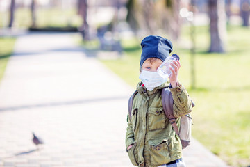 A boy in mask holds a bottle of water in hand