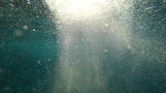 Air bubbles underwater slow coming up to the top of blue sea surface close up