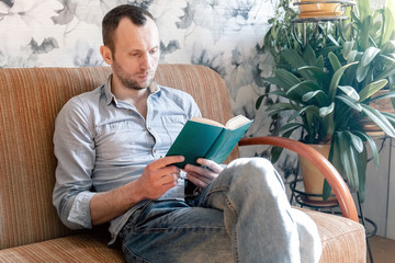 young man resting while sitting on a sofa with a book