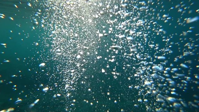 Air bubbles underwater slow coming up to the top of blue sea surface close up