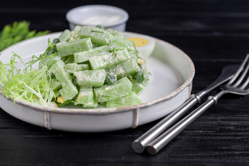 Salad of fresh cucumbers, spinach leaves, arugula, avocado. Served with slices of eggs and red pepper. Dietary nutrition. Breakfast for the whole family. Vitamin plate. On a dark wooden background.