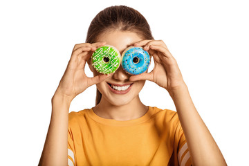 A beautiful, young girl holds two donuts in hand, blue and green. Woman wearing a yellow jersey and...
