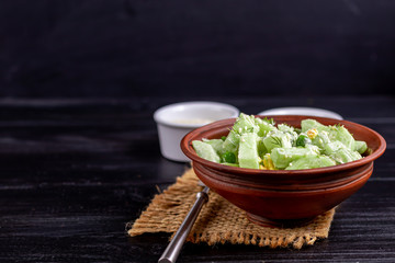 Salad of fresh cucumbers, spinach leaves, arugula, avocado. Served with slices of eggs and red pepper. Dietary nutrition. Breakfast for the whole family. Vitamin plate. On a dark wooden background.