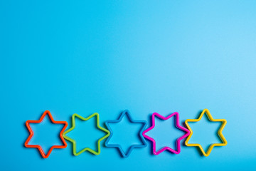 Five multi-colored plastic cookie cutter for making cookies in the shape of stars on a blue background. Culinary concept. Flat lay with copyspace.