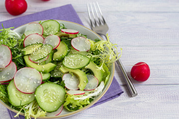 Salad of fresh cucumbers, spinach leaves, arugula, avocado. Served with slices of eggs and red pepper. Dietary nutrition. Breakfast for the whole family. Vitamin plate. On a dark wooden background.