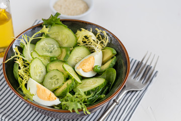 Salad of fresh cucumbers, spinach leaves, arugula, avocado. Served with slices of eggs and red pepper. Dietary nutrition. Breakfast for the whole family. Vitamin plate. On a light background.