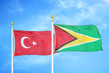 Turkey and Guyana two flags on flagpoles and blue cloudy sky