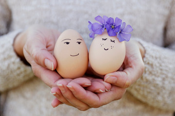 Woman holding cute egg couple with face and flowers wreath. Easter still life. Easter egg concept. Spring is coming. Holiday concept. Cute creative photo. 