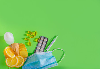 Coronavirus home treatment, medicine concept. Copy space. Stay home. Lemon and ginger,  Prevention face mask, pill capsules, thermometer and sanitizer on a green background.