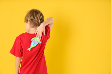 Little boy with paper fish on back against yellow background, space for text. April fool's day