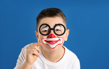 Preteen boy with clown makeup and party glasses on blue background. April fool's day
