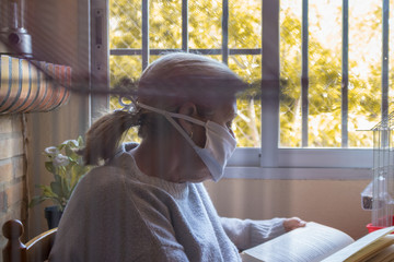 Mujer en el interior de su casa leyendo un libro mientras pasa la cuarentena