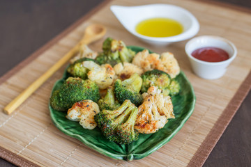Baked broccoli and cauliflower vegetables with spices on green plate. Vegan healthy diet food...