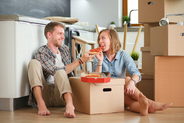 Fototapeta na wymiar Young couple have a pizza lunch break on the floor after moving into a new home with boxes around them. Young couple