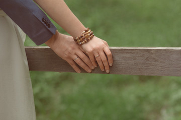 hands of a couple on the railing of a wooden bridge close-up