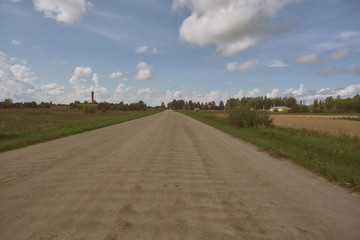 road in a field under a blue sky with clouds