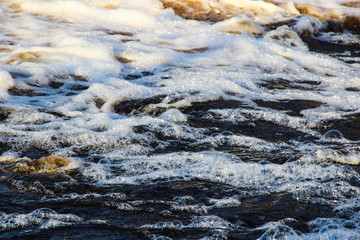 Water background. White water bubbles on water surface background, closeup. Blue water texture. Ripples on the water. Nature concept.