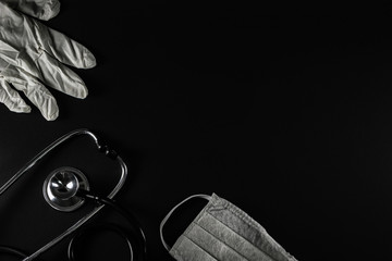 Diverse medical equipment on black background. Surgical protection face mask, rubber glove and stethoscope. Medical health care concept, top view, copy space.